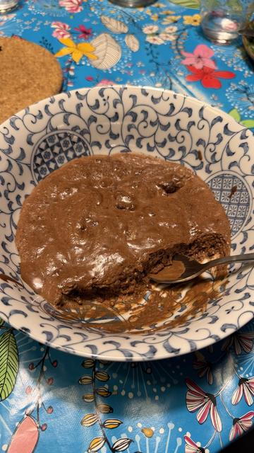 Une belle mousse au chocolat, marron, clair avec des bouts de chocolat visibles, dans un grand bol blanc et bleu avec plein de petits dessins, sur une table très colorée