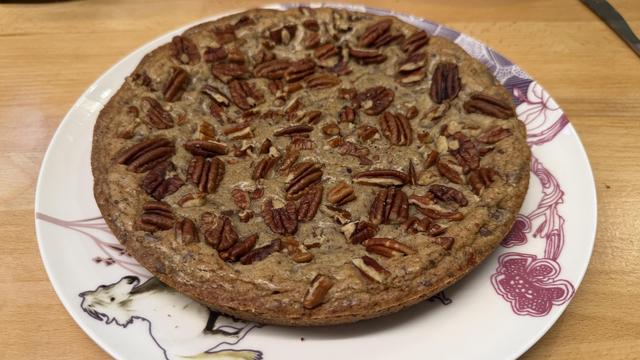 Un grand cookie qui prend toute une assiette. Il est couvert de noix de pécan 
