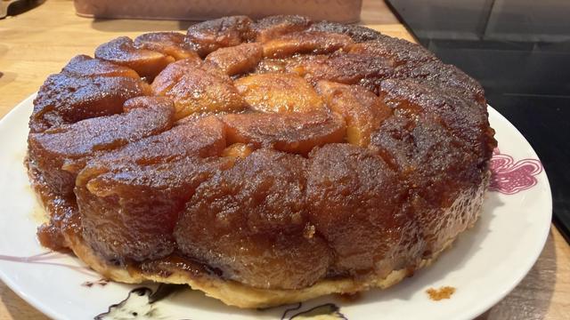 Une tarte Tatin en gros plan. On voit les pommes très caramélisées et généreuses. Elles sont très marrons et brillantes 