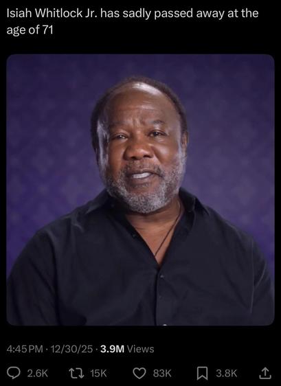 L’acteur Isiah Whitlock sur un fond violet. Il porte une chemise noire ouverte un peu au torse et sourit légèrement. 