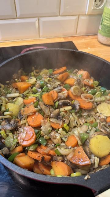 On voit une sauteuse remplie de légumes qui fument. On voit des carottes, des poireaux, des patates douces, des oignons et d’autres légumes.