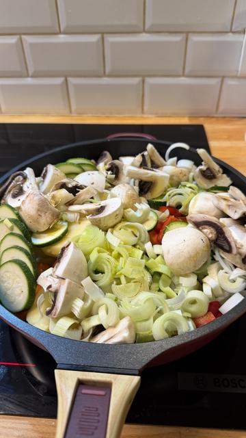 Une chanteuse avec deux dents, champignons, des pommes de terre, des oignons, des poireaux, des courgettes, etc. sur une plaque à induction en train de chauffer, mais encore cru