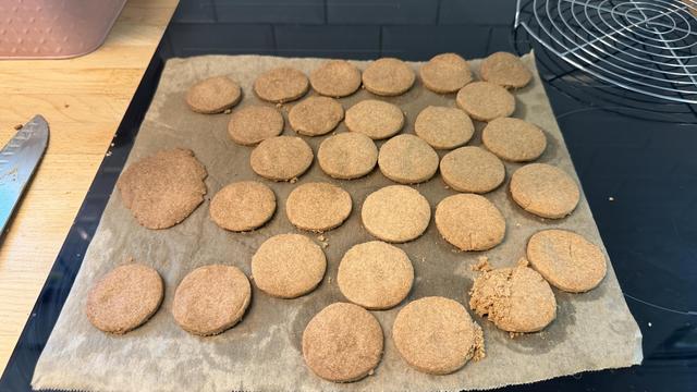 Plein de petits biscuits sablés coupés en gros ronds sur un papier cuisson qui est posé sur une plaque à induction pour refroidir 