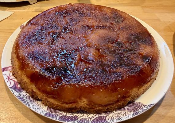 Une belle tarte, tatin, très caramélisée, avec les pommes aplaties au-dessus. La vue est plongeante, on voit un plan de travail en bois autour et des reflets sur les pommes.