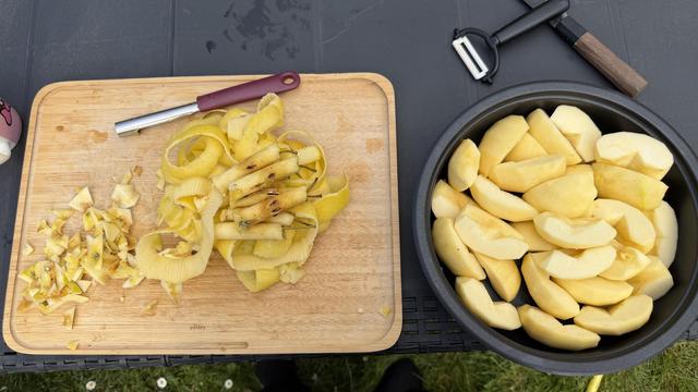 Une image d'une planche à découper en bois avec des pelures de pommes et des noyaux d'un côté, et un bol rempli de tranches de pommes pelées de l'autre côté. Un éplucheur est à proximité.
An image of a wooden cutting board with apple peels and cores on one side, and a bowl filled with peeled apple slices on the other side. A peeler is nearby.